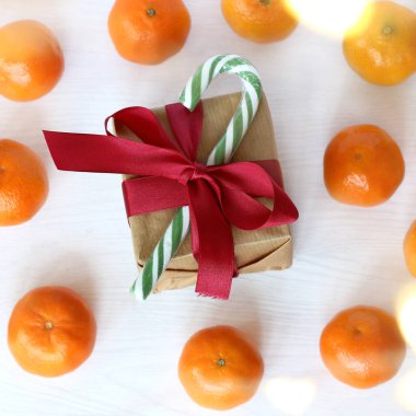 Çizgili şeker kadrosu, masa üstüne serpilmiş mandalinaların arka planında kırmızı bir fiyonk bulunan bir kutuyu dekore ediyor. Şenlik ortamında bir hediye.