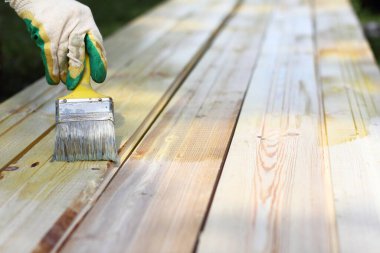 hand in a protective glove with a paint brush on the background of floor boards. painting with protective compound