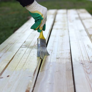 İşçi el, tahta döşeme tahtalarını boya fırçasıyla boyar. Ahşap yüzeylerin korunması