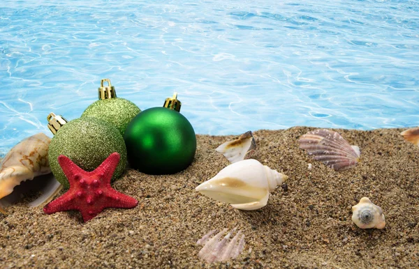 Christmas balls and shells on sand with summer sea background — Stock Photo, Image