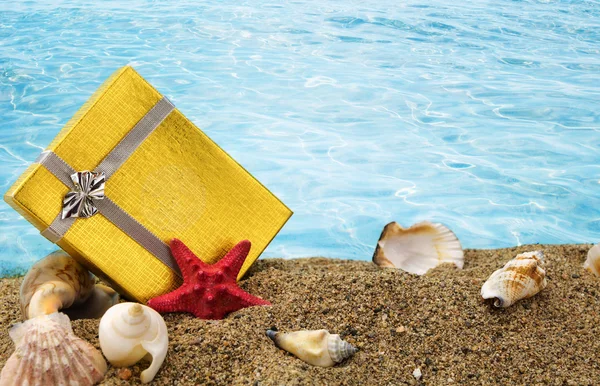Gold gift box on sand with summer sea background — Stock Photo, Image