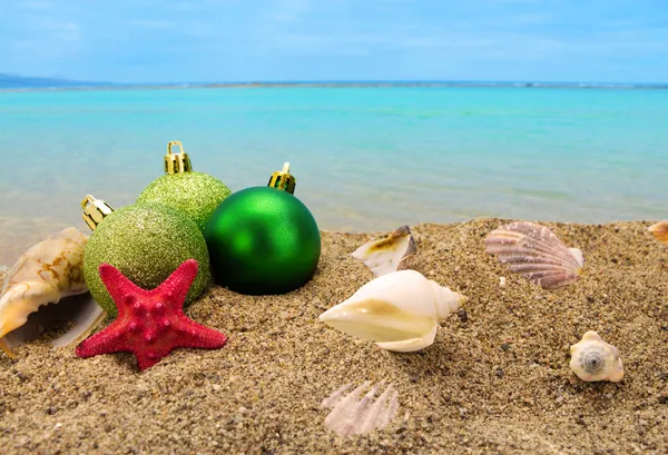 Bolas y conchas navideñas sobre arena con fondo marino de verano —  Fotos de Stock