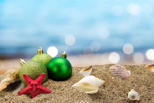Різдвяні кульки і мушлі на піску з літнім морським фоном — стокове фото