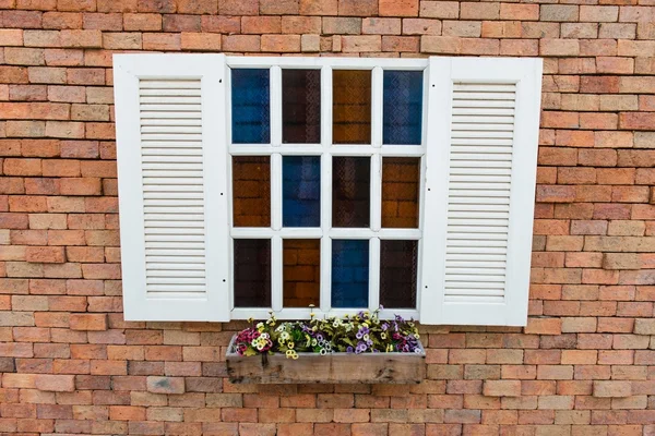 Wit venster frame op een rode bakstenen muur met bloemen — Stockfoto