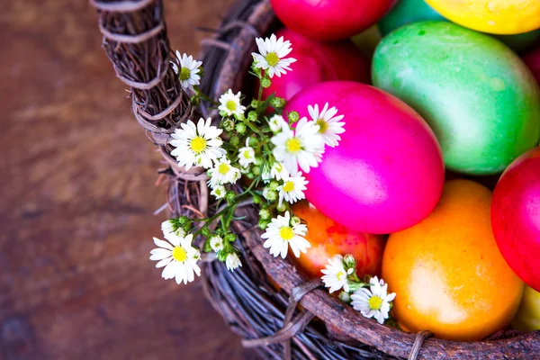 Colorful easter eggs in brown basket with flower — Stock Photo, Image