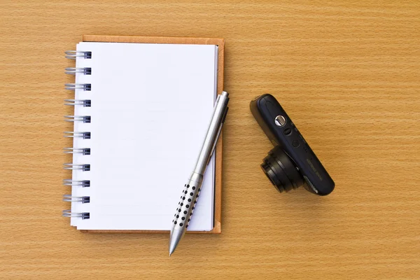 Note book and pen and camera. On the floor of the wooden table. — Stock Photo, Image