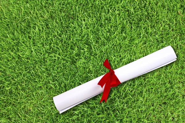 Diploma omwikkeld met een rood lint op verse lente groen gras — Stockfoto