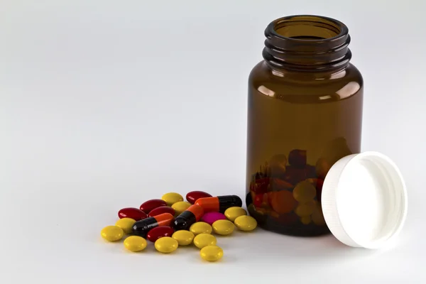 Comprimidos, comprimidos e cápsulas derramados de uma garrafa em branco backg — Fotografia de Stock