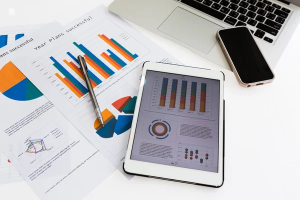 Gráficos financieros sobre la mesa con teléfono tableta y pluma —  Fotos de Stock