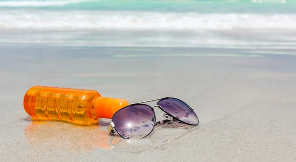 Sunscreen lotion and dark glasses on the beach for summer time — Stock Photo, Image