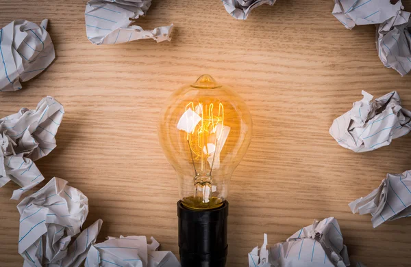 Glödlampa med skrynkligt papper på trä bakgrund — Stockfoto