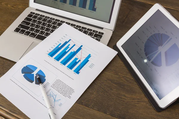 Финансовые диаграммы на столе с планшетом и ноутбуком — стоковое фото