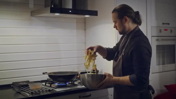Un homme dans un tablier prépare des nouilles dans un wok à la maison — Video