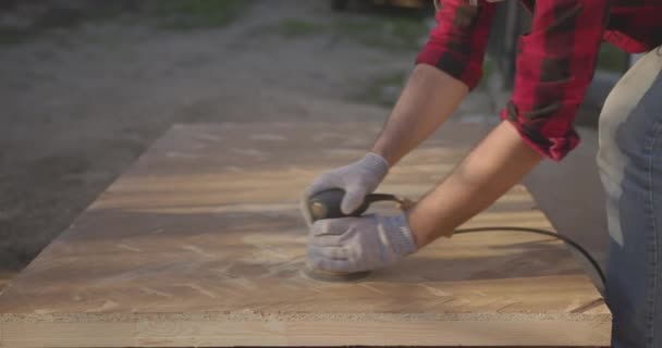 Een man met een masker, bril, polijst een parketplank met een schuurmachine.. — Stockvideo