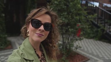 Genç, uzun kıvırcık saçlı, güneş gözlüklü kadın, sokakta selfie çekiyor.. 