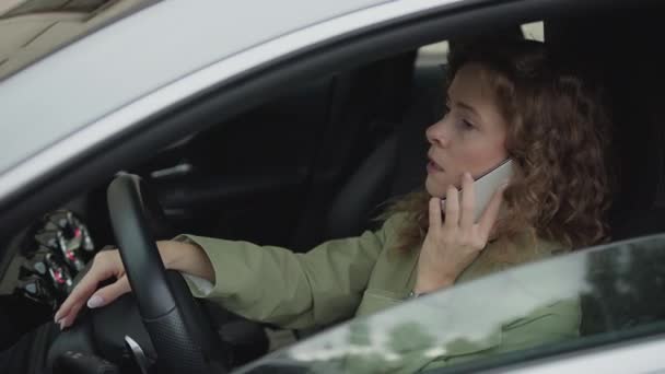 Молодая женщина напряженно разговаривает по телефону, находясь за рулем автомобиля — стоковое видео