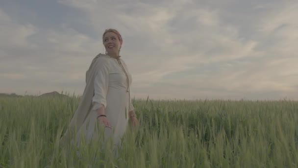 Uma jovem menina bonita em vestido étnico caminha ao longo do campo verde de trigo. — Vídeo de Stock