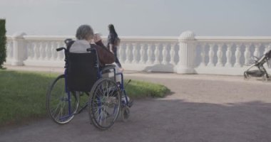 Yaşlı bir kadın deniz kenarında bir parkta oturuyor tekerlekli sandalyede kameraya doğru..