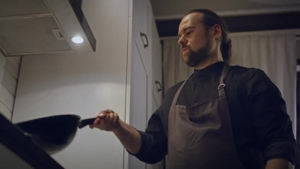 Girato di un uomo in un grembiule preparare il cibo sulla stufa in una padella o wok. — Video Stock