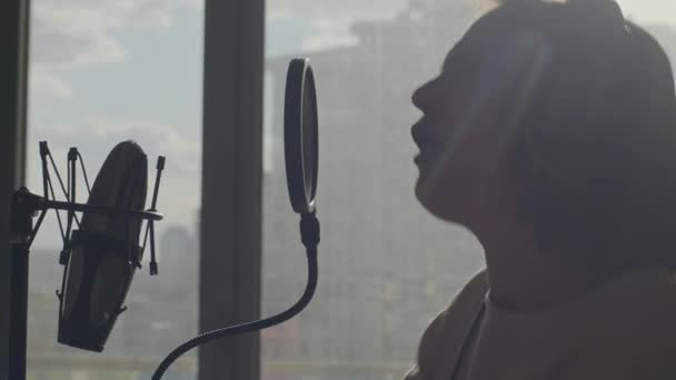 Uma jovem canta emocionalmente em um microfone no fundo da janela — Vídeo de Stock
