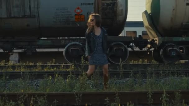 Une jeune fille marche le long du chemin de fer le long des wagons de marchandises. Concept d'aventure — Video