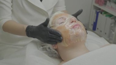 Güzellik salonunda bir kadın yüzüne nemlendirici bir doku maskesi takar..