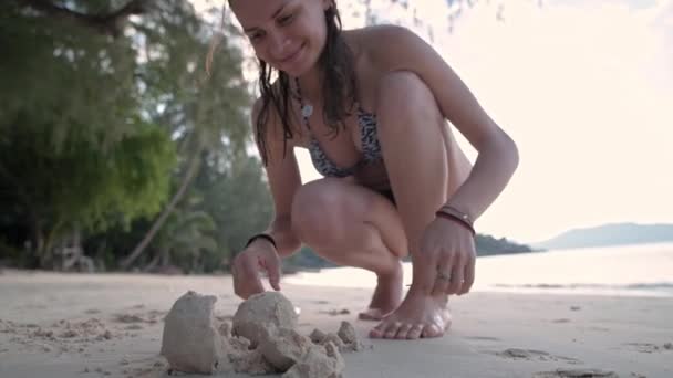 Девушка на пляже делает снеговика из песка. — стоковое видео