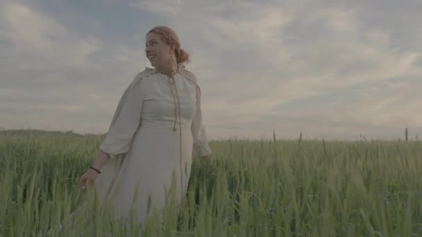 Молодая красивая девушка в этнической одежде ходит по зеленому полю пшеницы. — стоковое видео