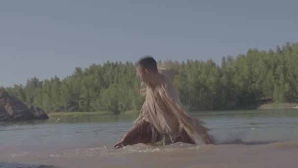 Een jonge mannelijke sjamaan danst een rituele dans die tot zijn knieën in een rivier staat — Stockvideo