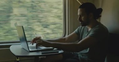 Genç beyaz erkek, tren kompartımanında dizüstü bilgisayarda çalışıyor..