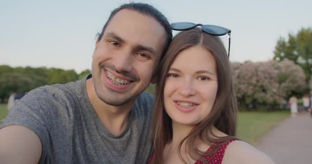 Un tânăr cuplu frumos de turiști cu aparate dentare fac selfie-uri în parc . — Videoclip de stoc