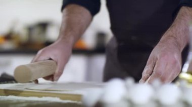 Hamur hazırlıklarına yakın çekim, erkek eli hamuru merdaneyle yuvarlıyor..