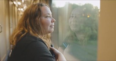 Genç tombul bir kız mutlu bir şekilde tren penceresinden dışarı bakar. Demiryolu yolculuğu.