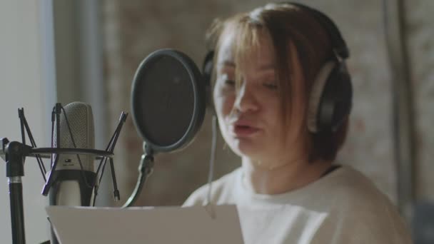 A young girl in monitor headphones in front of a microphone records a podcast — Stock Video