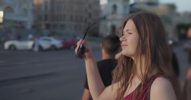 Flicka med långt hår står vid ett vägskäl. Sätter på solglasögon. solig sommardag — Stockvideo