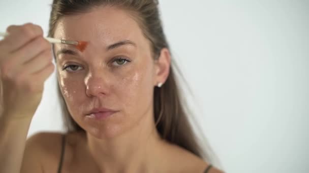 Uma menina bonita jovem aplica uma máscara hidratante transparente em seu rosto. — Vídeo de Stock