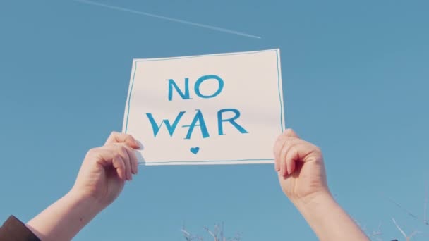 Close-up of a cardboard sign with the inscription no war on the blue sky — Stock Video