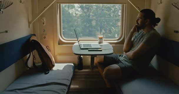 Genç beyaz bir adam trenle seyahat ederken kulaklıkla oturur.. — Stok video