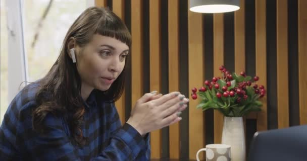 Portrait of a young girl in headphones talking in front of a laptop screen. — Stock Video