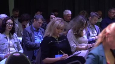 Dinleyiciler konferans salonundaki konuşmacının konuşmasını dinliyor.