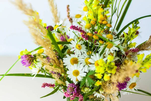 A bouquet of wild flowers in a small glass vase on a white background. Stylish appearance, layout, personality. Banner, a place for the text. Background for advertising and presentation.