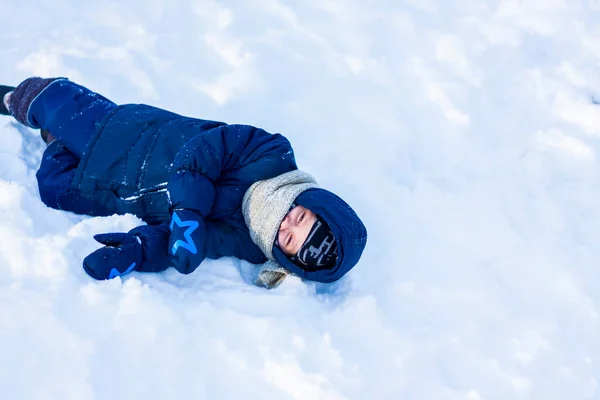 在一个阳光灿烂的冬日里 一个笑容满面的孩子躺在雪地里 很多雪和非常寒冷 积极的冬季户外运动 快乐圣诞假期的概念 — 图库照片