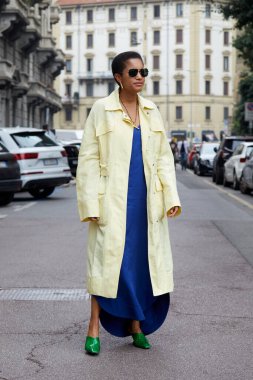 MILAN, İtalya - 25 Eylül 2021: Tamu McPherson soluk sarı, uzun paltolu, elektrik mavisi elbiseli ve yeşil uçlu ayakkabılı Salvatore Ferragamo defilesinden önce, Milan Moda Haftası tarzı
