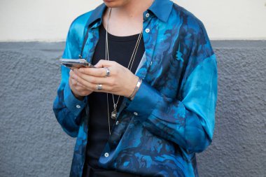 MİLAN, İtalya - 18 Haziran 2022: Milano 'daki Marcelo Burlon County defilesinden önce akıllı telefona bakan mavi kamuflaj gömlekli adam, Milan Moda Haftası tarzı