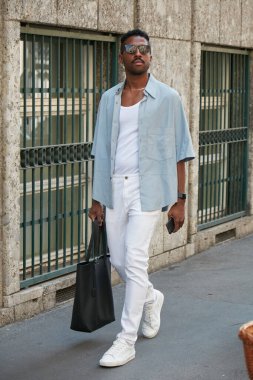 MILAN, ITALY - JUNE 20, 2022: Man with pale blue shirt, white trousers and sneakers before Giorgio Armani fashion show, Milan Fashion Week street style