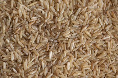Long-grained brown rice, a highly nutritious gluten-free whole grain used in a variety of dishes and a great source of dietary fiber and vitamins; background of raw dried food flat lay with copy space