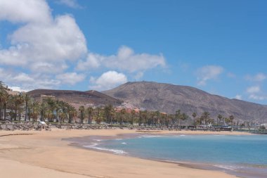 Playa de el Camison, Las Americas, Tenerife, Kanarya Adaları, İspanya - 3 Haziran 2020: Uzun altın plaj şemsiyeleri ve popüler tatil köyünün yakınındaki şezlonglar, turist olmadan boş