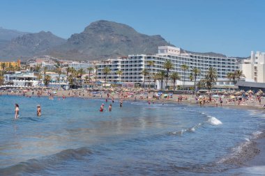 Playa de Troya, Costa Adeje, Tenerife, Kanarya Adaları, İspanya - 1 Mayıs 2022: Sıcak dalgaların, güneşlenmenin ve otellere ve diğer tesislere yakın olmanın keyfini çıkaran birçok turistin bulunduğu popüler plaj