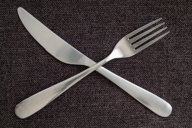 Crossed fork and knife on a gray tablecloth representing taking a break, silverware arranged in symbolic way on table, combination of neat and clean cutlery, close-up overhead shot of eating utensils