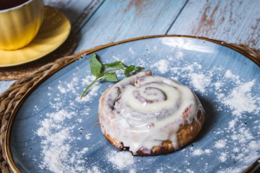 Mavi tabakta ev yapımı Cinnabon Bun ve çayla birlikte sarı bardak. Seçici odak